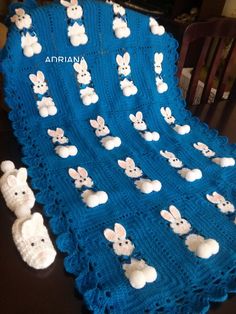 a crocheted blanket that has white rabbits on it and is sitting on a table