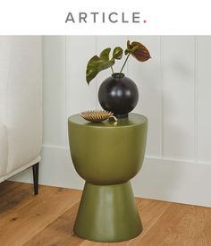 a vase sitting on top of a green table next to a black vase with a plant in it