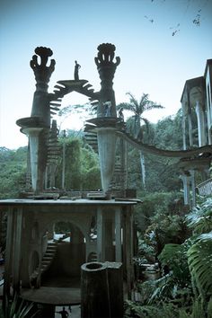 an old building with statues on top of it in the middle of trees and bushes