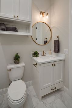 a white toilet sitting next to a sink in a bathroom under a large round mirror