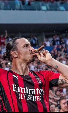 a man in a red and black shirt eating a hot dog at a sporting event