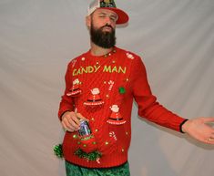 a man with a beard wearing an ugly christmas sweater and green pants, holding a can of candy man