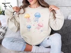 Jellyfish and Stars Graphic Sweatshirt Materials: Sweatshirts and hoodies are made of 50% cotton and 50% polyester. T-shirts in solid colors are 99% cotton and 1% polyester, while t-shirts in heather and blended colors are 52% cotton and 48% polyester. Cancellations: Accepted within 2 hours of your purchase. Shipping: Orders typically ship within 4 business days, though most are shipped the next day. Once the order ships, delivery usually takes 1-5 days depending on your location. Returns/Exchanges: All orders are made-to-order, so we do not accept returns or exchanges. However, please contact us if you have any issues with your order. Care Instructions: Machine wash cold, tumble dry on low heat. Do not dry clean or iron the design directly. Thank you for shopping with Luveana! Jellyfish Hoodie, Space-themed Cotton Crew Neck Top, Jellyfish T Shirt, Dolphin Sweatshirt, Cheap Crew Neck T-shirt With Fish Print, Ocean Themes, Jellyfish, Beach Outfit, Cute Designs