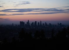 the city skyline is lit up at night with clouds in the sky and trees below