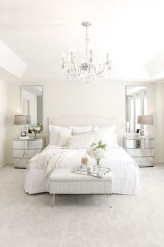 a white bedroom with chandelier, bed and mirror on the wall above it