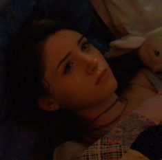 a woman laying in bed with her head on the pillow and holding a stuffed animal