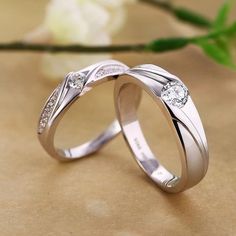 two white gold wedding rings with diamonds on top of each other next to a flower