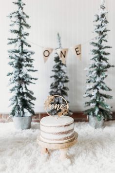 a white cake sitting on top of a wooden stand next to evergreen trees and bunting