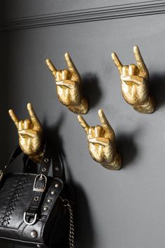 three gold hand - shaped hooks hang on the wall next to a black purse