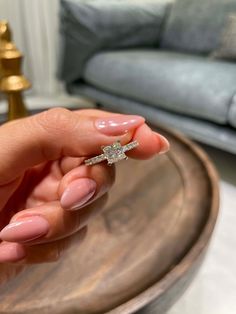 a woman's hand holding a diamond ring on top of a table in front of a couch