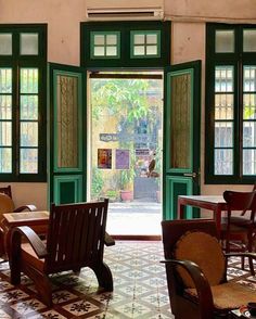 an open door leading into a restaurant with green doors and chairs in front of it