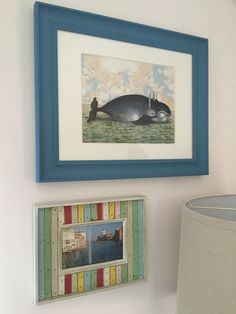 a blue framed whale is hanging on the wall next to a lamp and photo frame