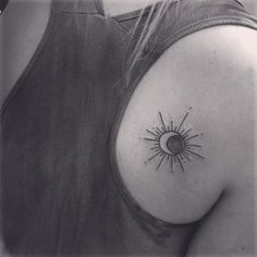 a black and white photo of a woman's shoulder with a sun tattoo on it