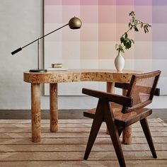 a table with a chair, lamp and vase on it in front of a colorful wall