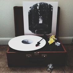 a record player sitting on top of an old suitcase with a yellow flower next to it