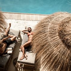 two men lounging on chaise lounges next to the ocean and straw umbrellas