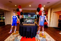 two young men standing in front of a table with balloons and basketballs on it