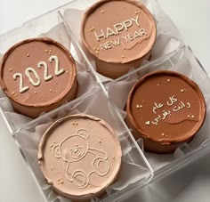 four cupcakes with happy new year written on them in plastic cases and decorated with icing