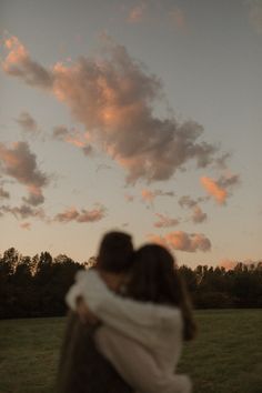 a man and woman embracing each other in the middle of a field under a cloudy sky