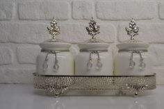 three white glass jars with crystal decorations on them are sitting on a silver stand in front of a brick wall