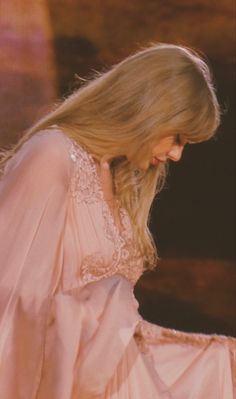 a woman with blonde hair wearing a pink dress and holding her hand on her hip