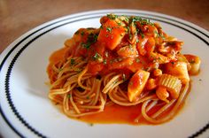 a white plate topped with pasta and meat covered in sauce on top of a wooden table