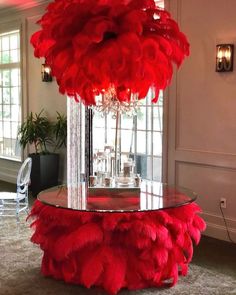 a table with red feathers on it in front of a chandelier and chairs