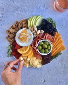 a platter filled with meats, cheeses, fruit and crackers is being held by a person's hand