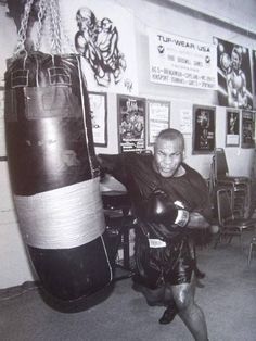 an old photo of a man wearing boxing gloves and holding a punching bag in a gym