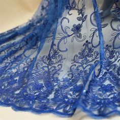 the blue lace is on top of the white cloth with flowers and leaves in it