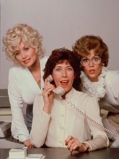 three women sitting at a table talking on the phone and one is holding a cellphone to her ear