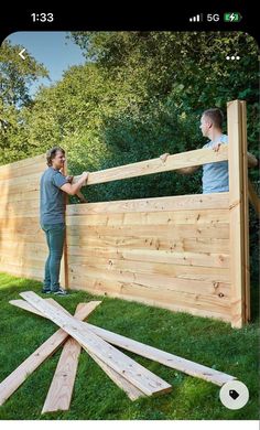 two men are building a wooden fence in the yard with wood planks on the grass