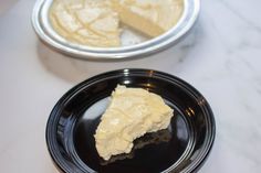 a piece of cake on a black plate next to a silver bowl with white frosting