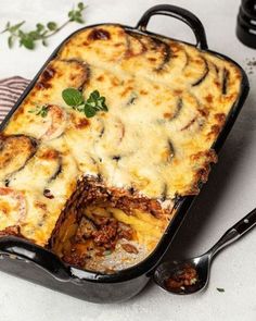 a casserole dish with meat and cheese in it on a table next to two spoons