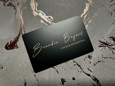 a black business card sitting on top of a table covered in dirt and water droplets