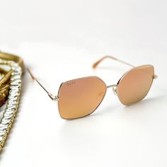 A pair of gold tone sunglasses with peach orange mirror lenses. Pictured on a white background with gold jewelry. Trendy Sunglasses With Uva Protection For Travel, Trendy Aviator Sunglasses With Uva Protection For Travel, Trendy Sunglasses With Tinted Lenses For Everyday, Trendy Metal Frame Sunglasses For Everyday Use, Trendy Mirrored Sunglasses For Travel, Mirrored Lenses Sunglasses For Everyday Summer Use, Summer Travel Sunglasses With Metal Frame, Peach Mirror, Retro Shades