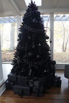 a black christmas tree with presents under it in a room filled with windows and wood flooring