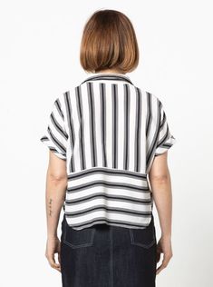 a woman standing in front of a white wall wearing a black and white striped shirt