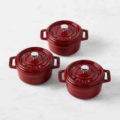 three red pots sitting on top of a white counter next to each other and one has a lid