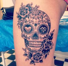 a woman's thigh with a sugar skull and roses tattoo on her leg,