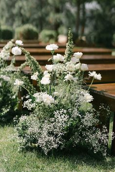 rows of wooden benches with white flowers in the grass on each side and greenery behind them