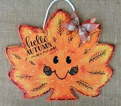 an orange leaf with a bow hanging from it's side and the words hello autumn painted on it