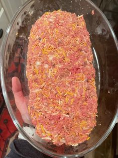 a person holding up a large meatloaf in a glass bowl with mustard sprinkled on it