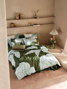 a bed with green and white comforter in a room next to a shelf filled with vases