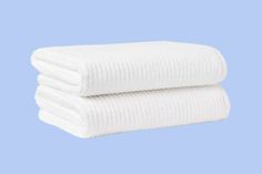 two white towels stacked on top of each other in front of a light blue background