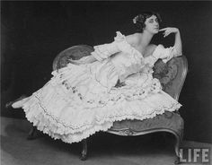 an old black and white photo of a woman in a dress sitting on a chair