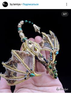 a hand holding a gold and green beaded dragon headpiece with beads on it