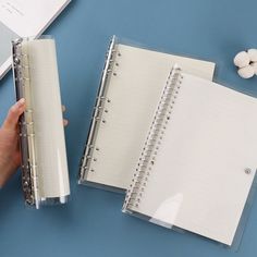 a hand holding a binder next to two notebooks on a blue table top