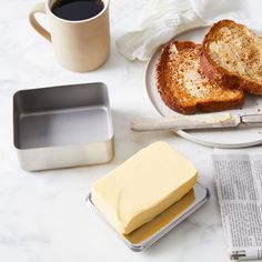 two slices of bread, butter and coffee on a white plate with newspaper next to it