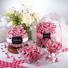 pink candies in small glass bowls on a table with flowers and ribbons around them